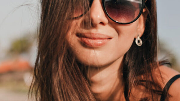 feche-o-retrato-de-uma-mulher-muito-feliz-com-cabelo-escuro-usando-oculos-escuros-pretos-posando-durante-a-sessao-de-fotos-na-praia-perto-do-oceano